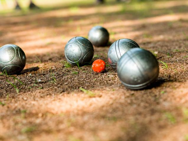 Gleise mit silbernen Boulekugeln und einer roten Kugel auf einem erdigen Boden in einem Park.