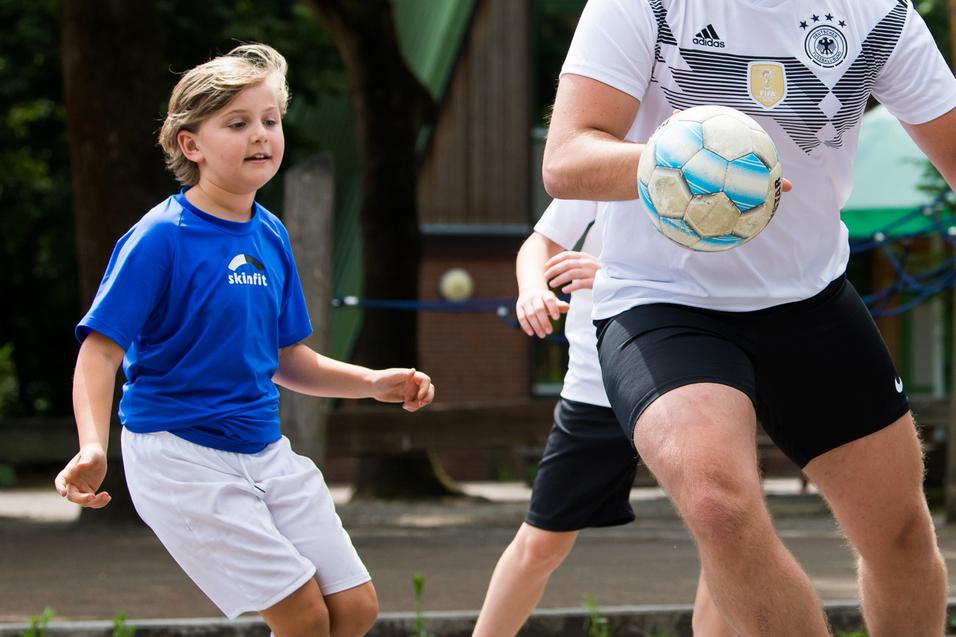 Ein Junge in blauer Sportkleidung dribbelt einen Ball, während ein älterer Spieler ihm entgegenkommt.