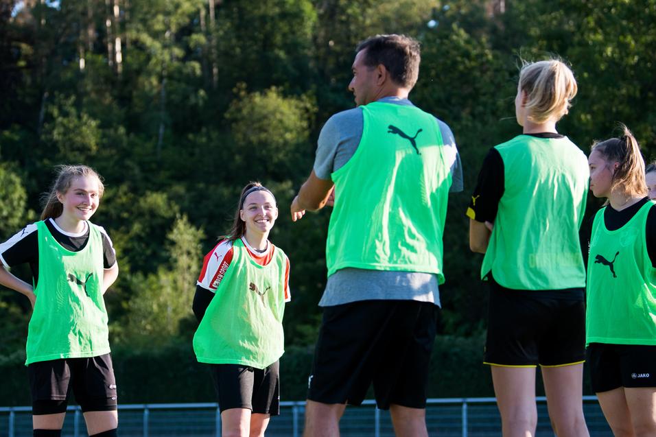 Mannschaftstraining mit Trainer: Gruppen von Mädchen tragen grüne Trainingswesten auf einem Fußballplatz.
