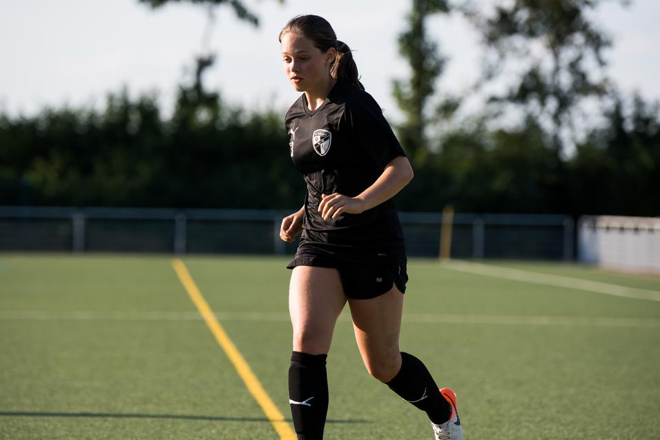 Eine Frau in schwarzer Sportkleidung dribbelt einen Fußball auf einem Kunstrasenplatz.