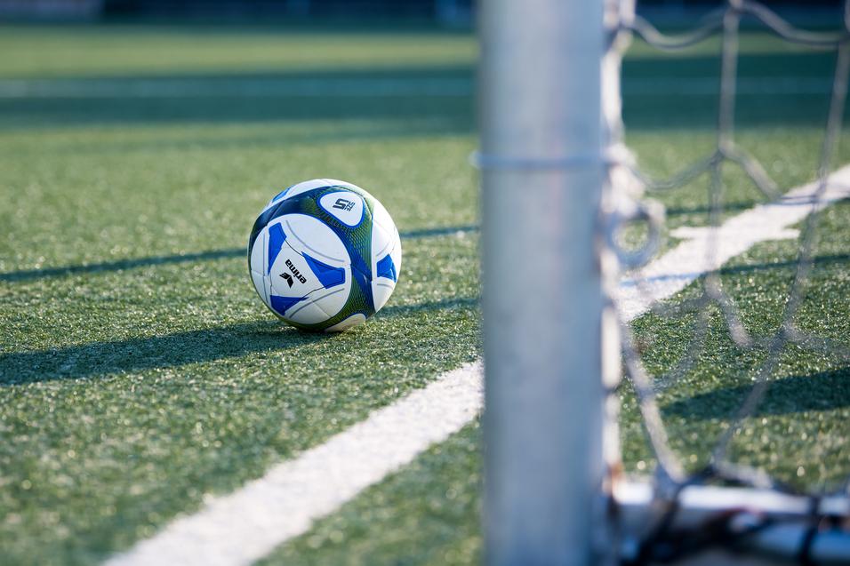 Fußball liegt auf einem Kunstrasenplatz, nahe einem Torpfosten mit Netz.