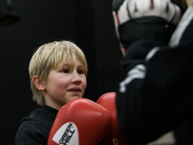Junger Boxer mit blondem Haar trägt rote Handschuhe und lächelt während des Trainings in einem Sportstudio.