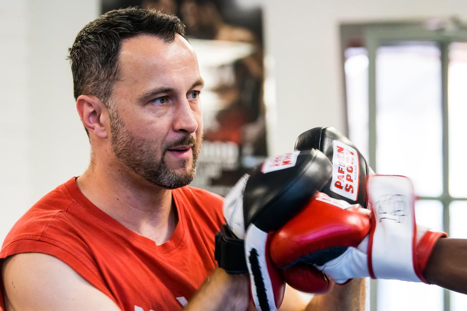 Trainer überwacht das Boxtraining eines Schülers, beide tragen Boxhandschuhe in einem Trainingsraum.