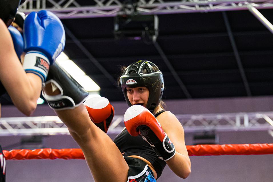 Kämpferin im Boxring mit Kopfschutz und roten Handschuhen hebt ihr Bein für einen Kick.