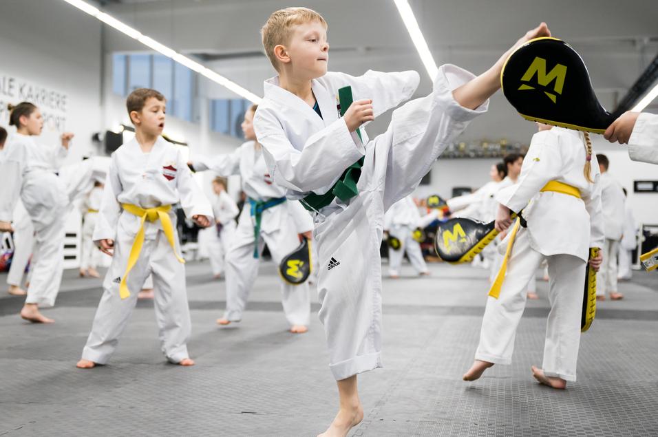 Eine Gruppe von Kindern in Karate-Uniformen übt in einem Trainingsraum, ein Junge führt einen Kick aus.