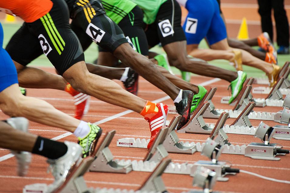 Start einer Sprintveranstaltung mit mehreren Athleten in Blockstartposition auf einer Laufbahn.