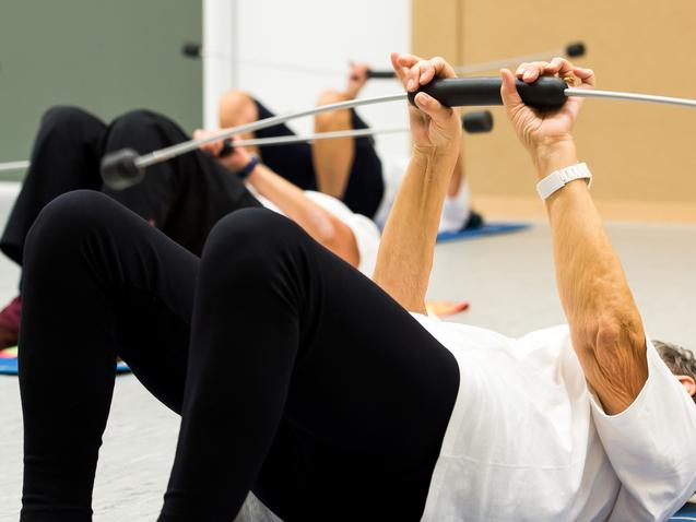 Ältere Personen machen auf Gymnastikmatten Liegestütze mit Widerstandsband in einem Trainingsraum.