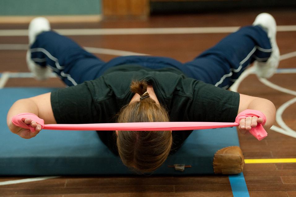 Frau führt eine Übung mit einem pinken Widerstandsband auf einer Matte in einem Sportbereich aus.