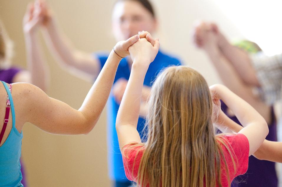 Gruppe von Kindern hält sich in einem gemeinsamen Kreis an den Händen, während sie in einer Sporthalle aktiv sind.