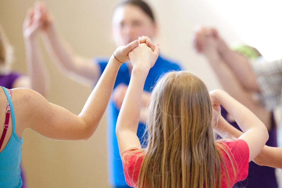 Gruppe von Kindern hält sich in einem gemeinsamen Kreis an den Händen, während sie in einer Sporthalle aktiv sind.