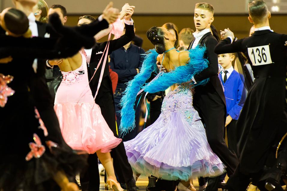 Tanzpaare in eleganten Kostümen tanzen auf einem Parkettboden bei einem Tanzwettbewerb.