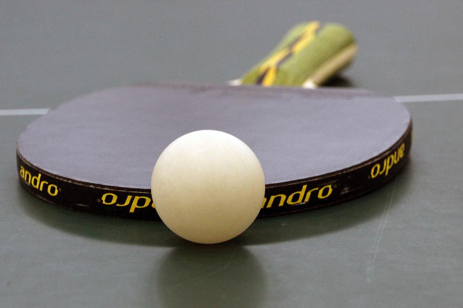 Nahaufnahme eines Tischtennisschlägers mit weißem Ball auf einer grünen Tischtennisplatte.