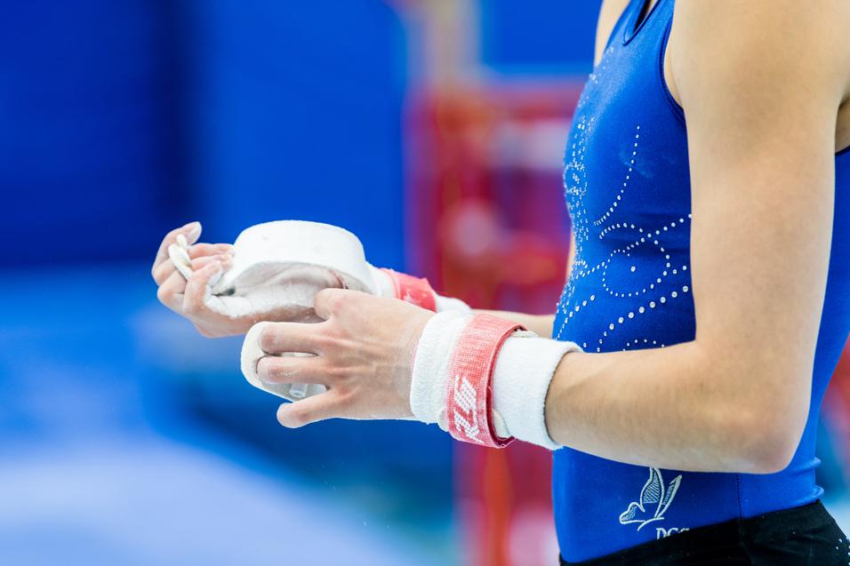 Nahaufnahme einer Sportlerin mit Kreide in der Hand, die ihre Hände mit einem roten Handgelenkschutz umwickelt.