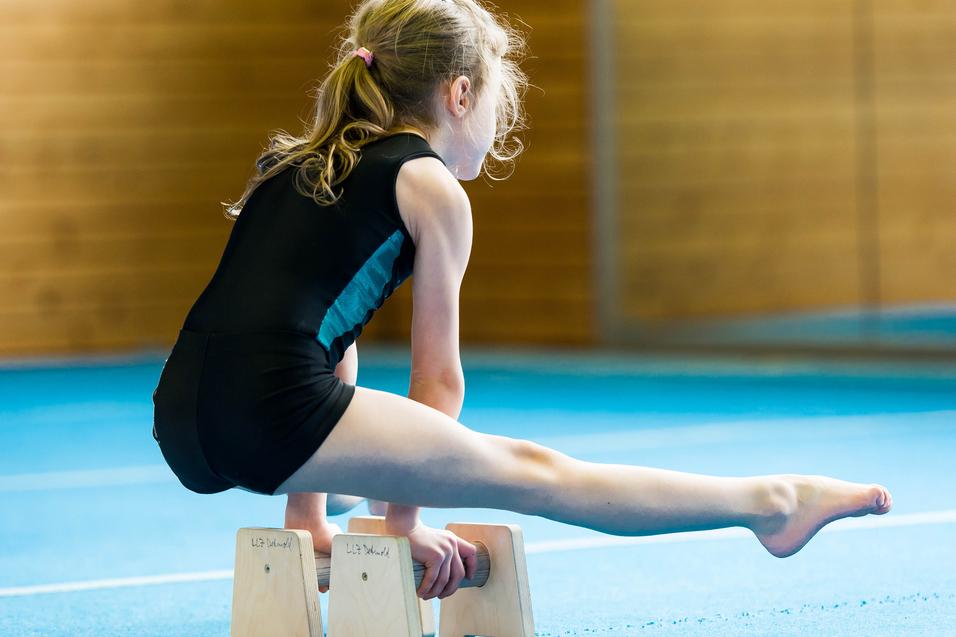 Mädchen in Turnkleidung balanciert auf Holzblöcken während des Trainings in einer Turnhalle.