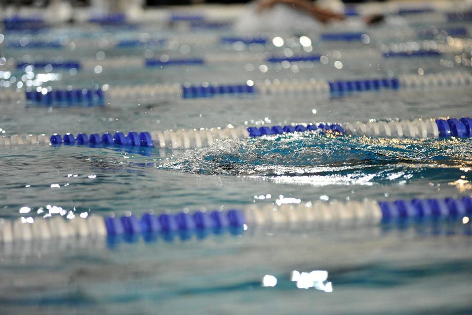Spritzendes Wasser auf einer Schwimmbahn mit blauen und weißen Bahnmarkierungen in einem Hallenbad.