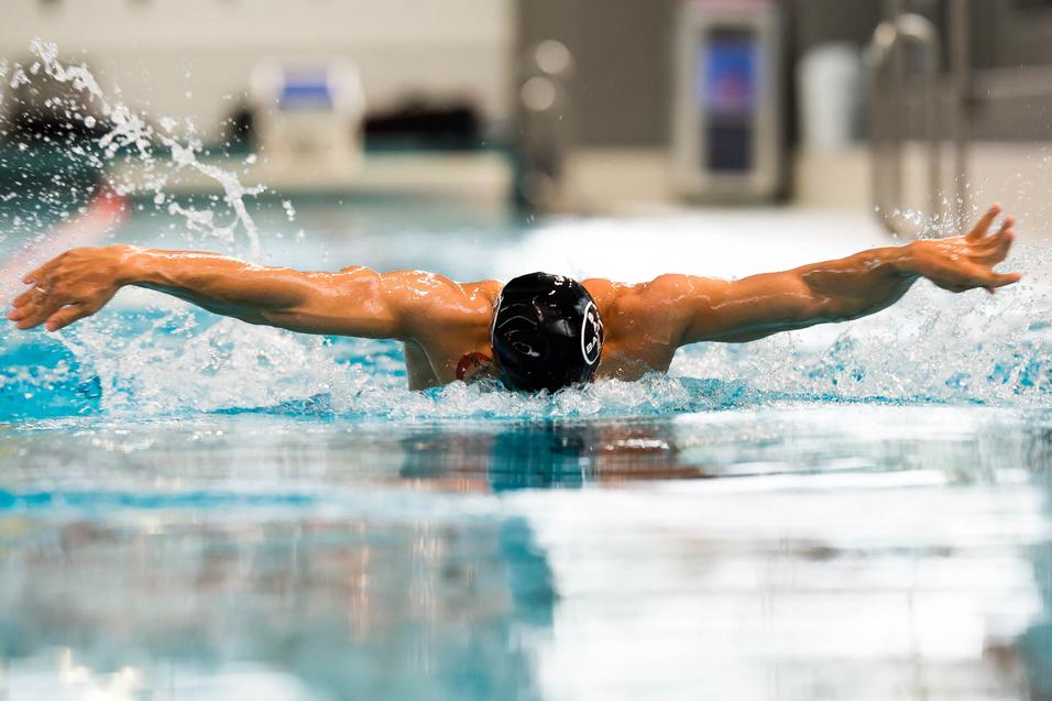 Schwimmer bei der Schmetterlingsbewegung im Wasser, Arme weit ausgebreitet, Spritzer um ihn herum.