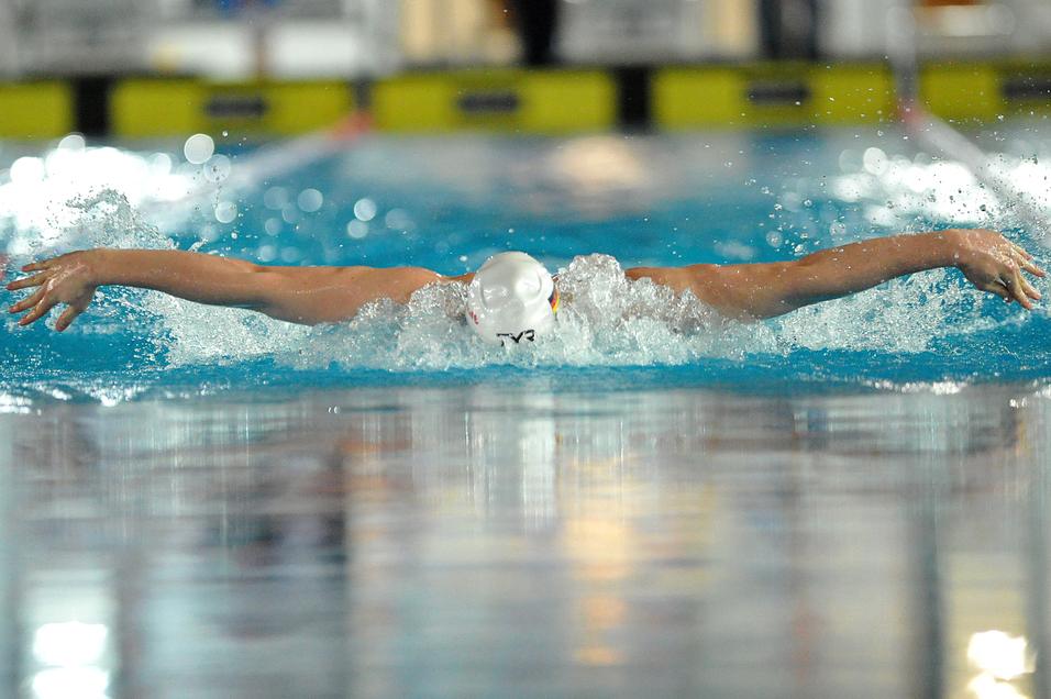 Schwimmer führt einen Butterfly-Zug im Wasser aus, Hände und Kopf über der Wasseroberfläche.
